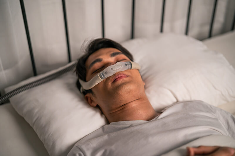 Homem dormindo confortavelmente com CPAP nasal discreto